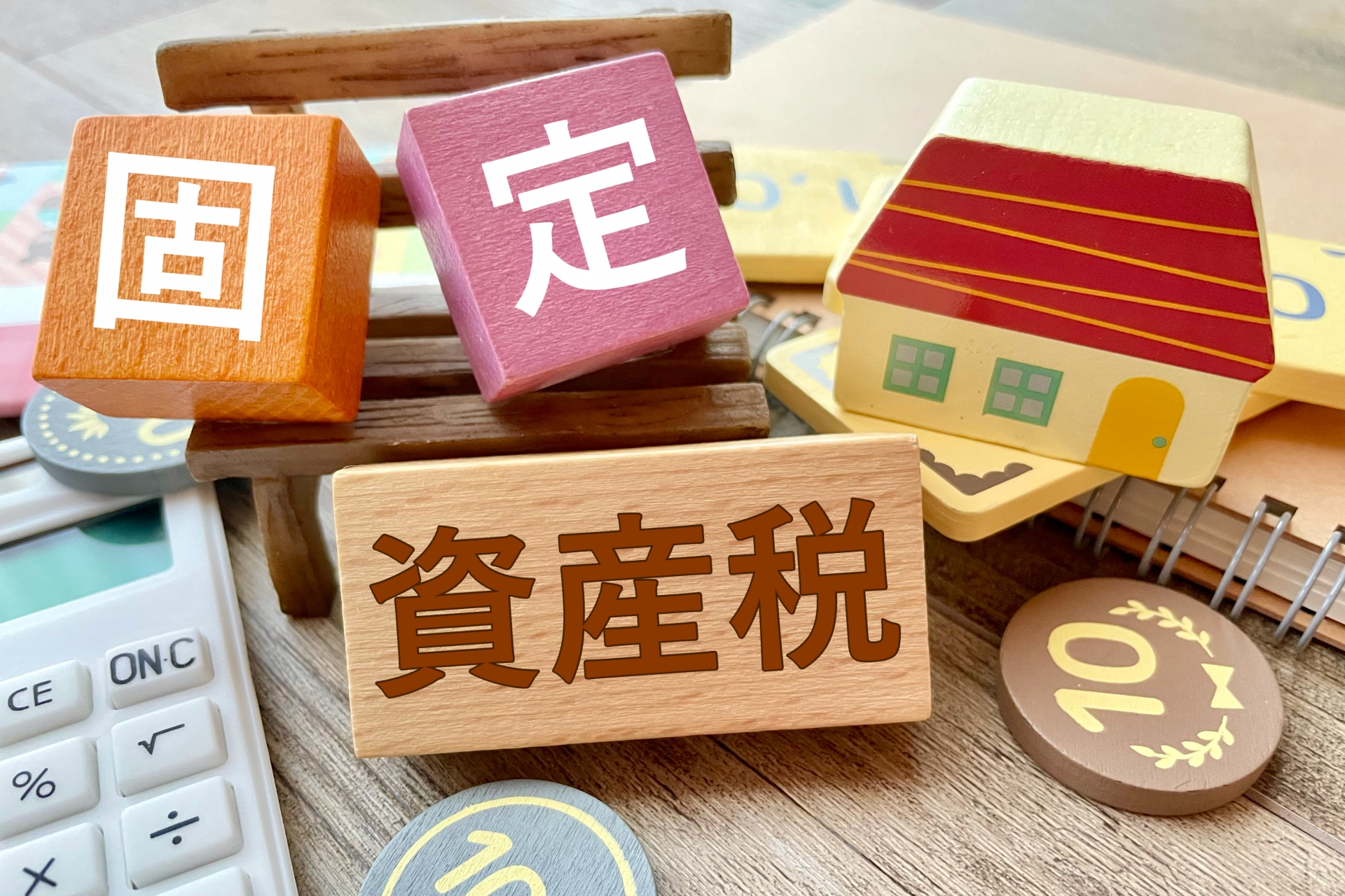 不動産売却時の税金、固定資産税の文字と家の模型、電卓を配置したビジネスイメージ