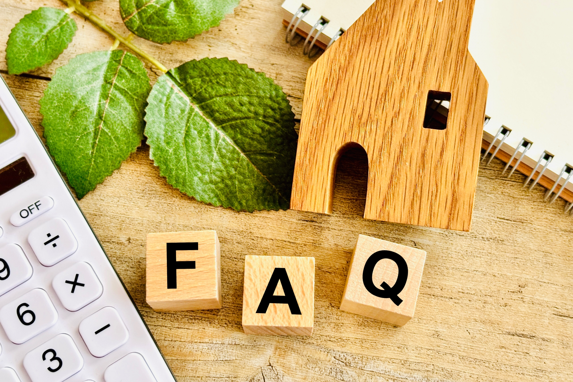 不動産売却のよくある質問（FAQ）。木の家、電卓、FAQの文字で疑問解決を表現