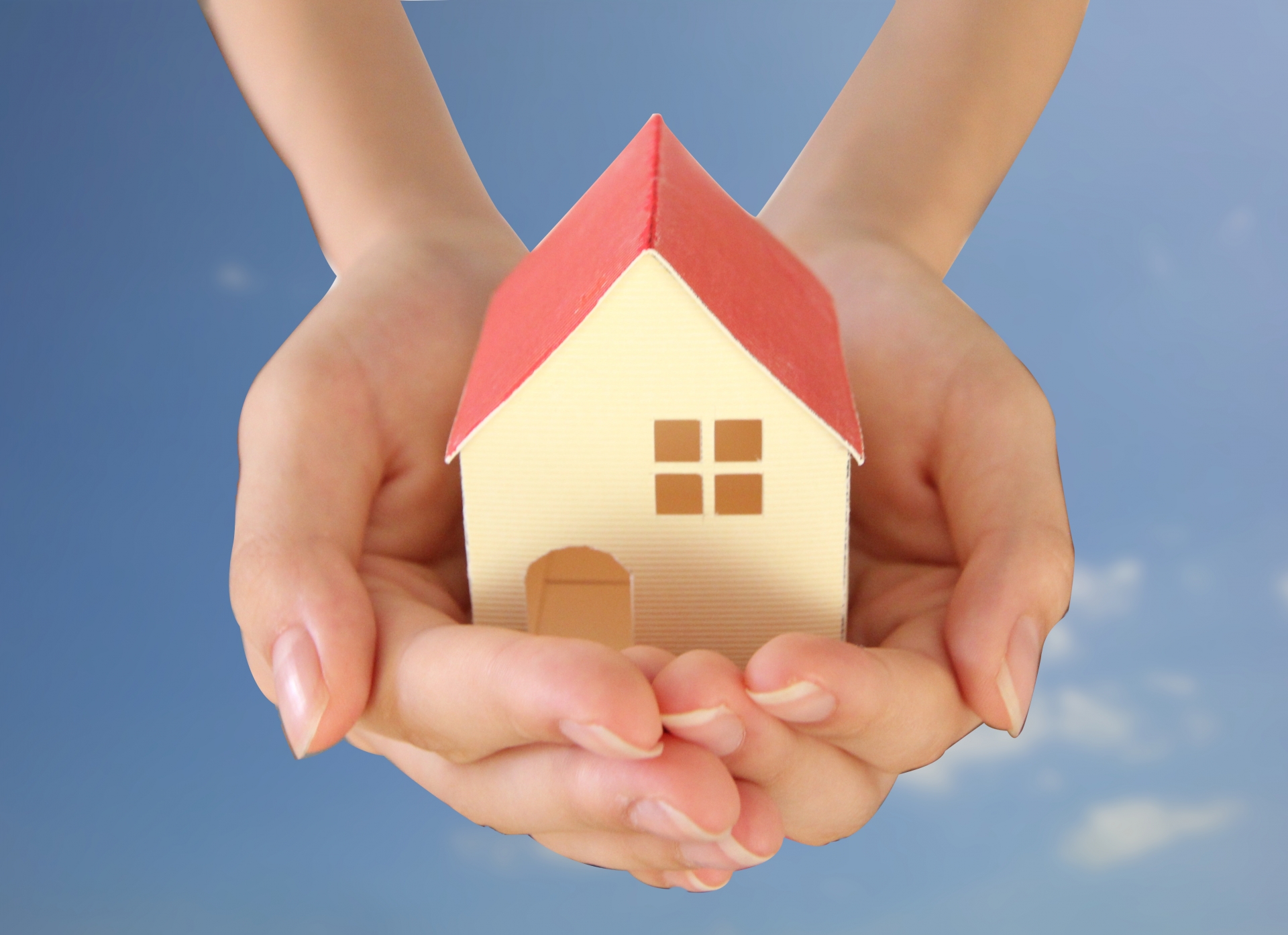 不動産売却やマイホームの安心感を表現。両手で小さな家を包み込むイメージ