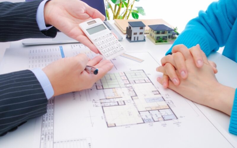 不動産売買における費用の計算や契約の流れを、電卓と間取り図を用いて顧客に説明する担当者