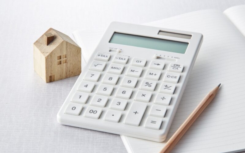 不動産売買にかかる費用の計算や、住宅ローンの返済計画に用いる白い電卓と家の模型