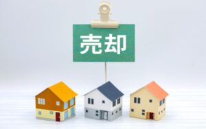 家を高く売る最適なタイミングを探る、「売却」の看板と並んだ戸建て住宅のミニチュア