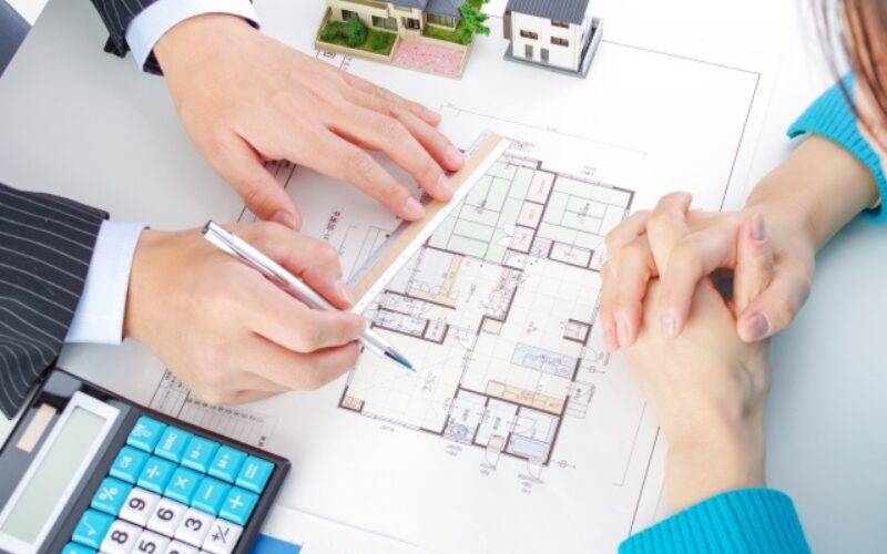 住み替えで家が売れない時の対処法として、間取り図と電卓を使い売却戦略を話し合う担当者と相談者