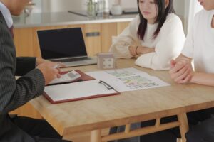 不動産売買について、担当者が若い夫婦に対し、間取り図を見ながら契約内容を詳しく説明している様子。