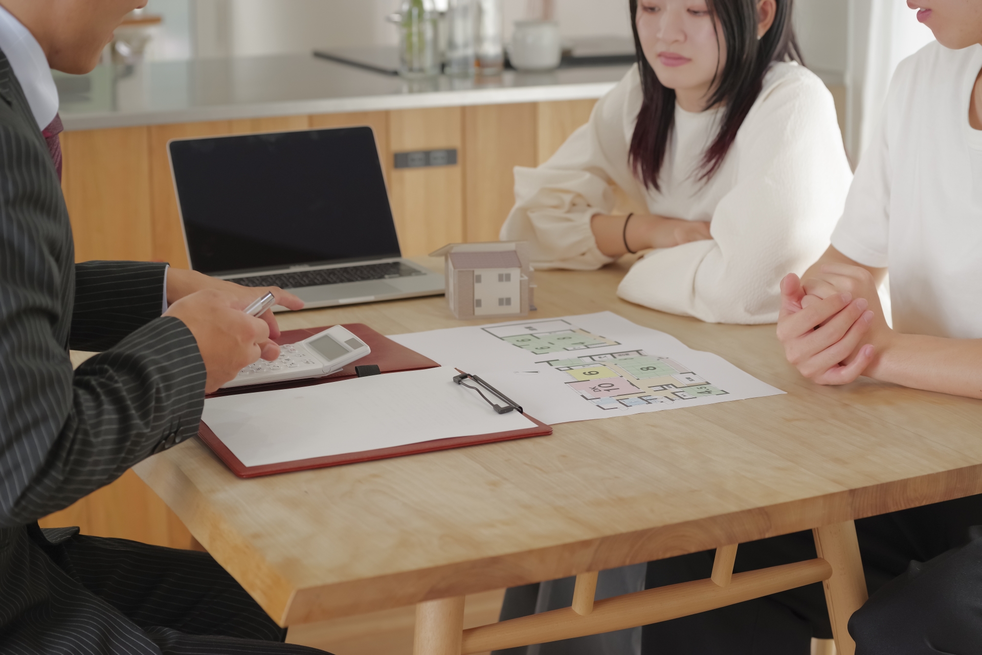 不動産売買について、担当者が若い夫婦に対し、間取り図を見ながら契約内容を詳しく説明している様子。