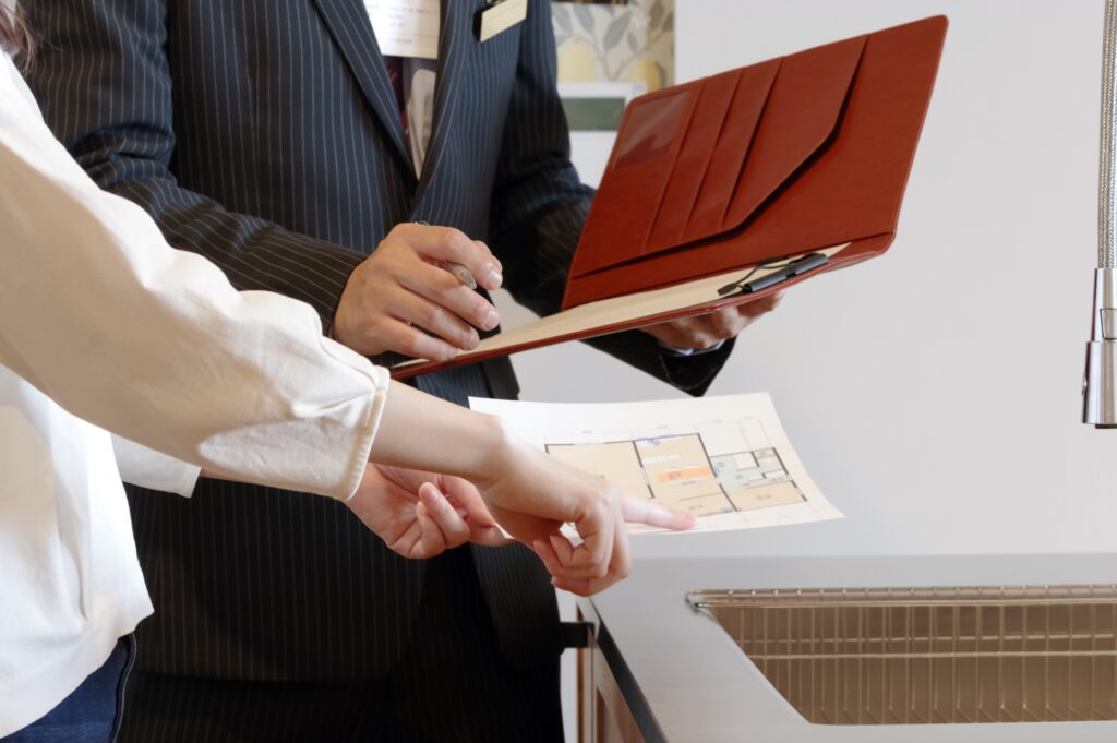 カウンター越しに、スーツ姿の担当者と顧客が間取り図を指差し、内容を確認している。