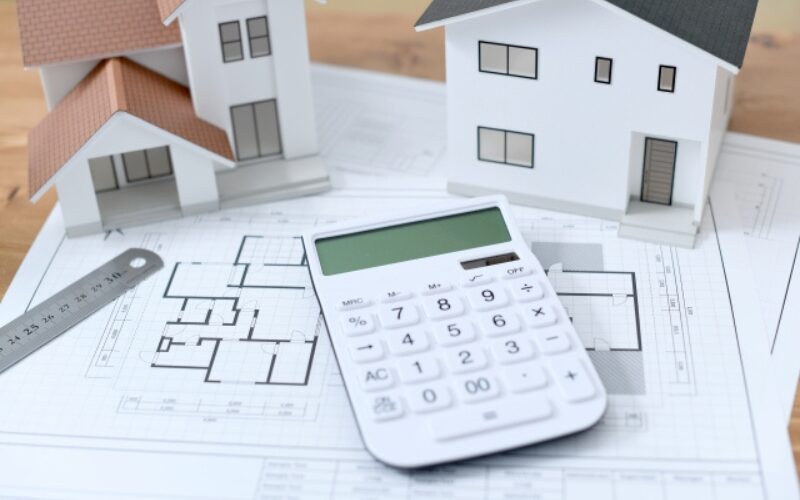 家が売れない際のリスクとして価格見直しを行う、家の模型と設計図、電卓による売却検討のイメージ