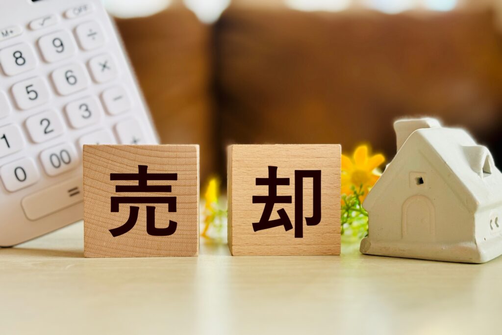 古い家を売却する際の計算をイメージした、電卓、木製ブロック、ミニチュアの家。