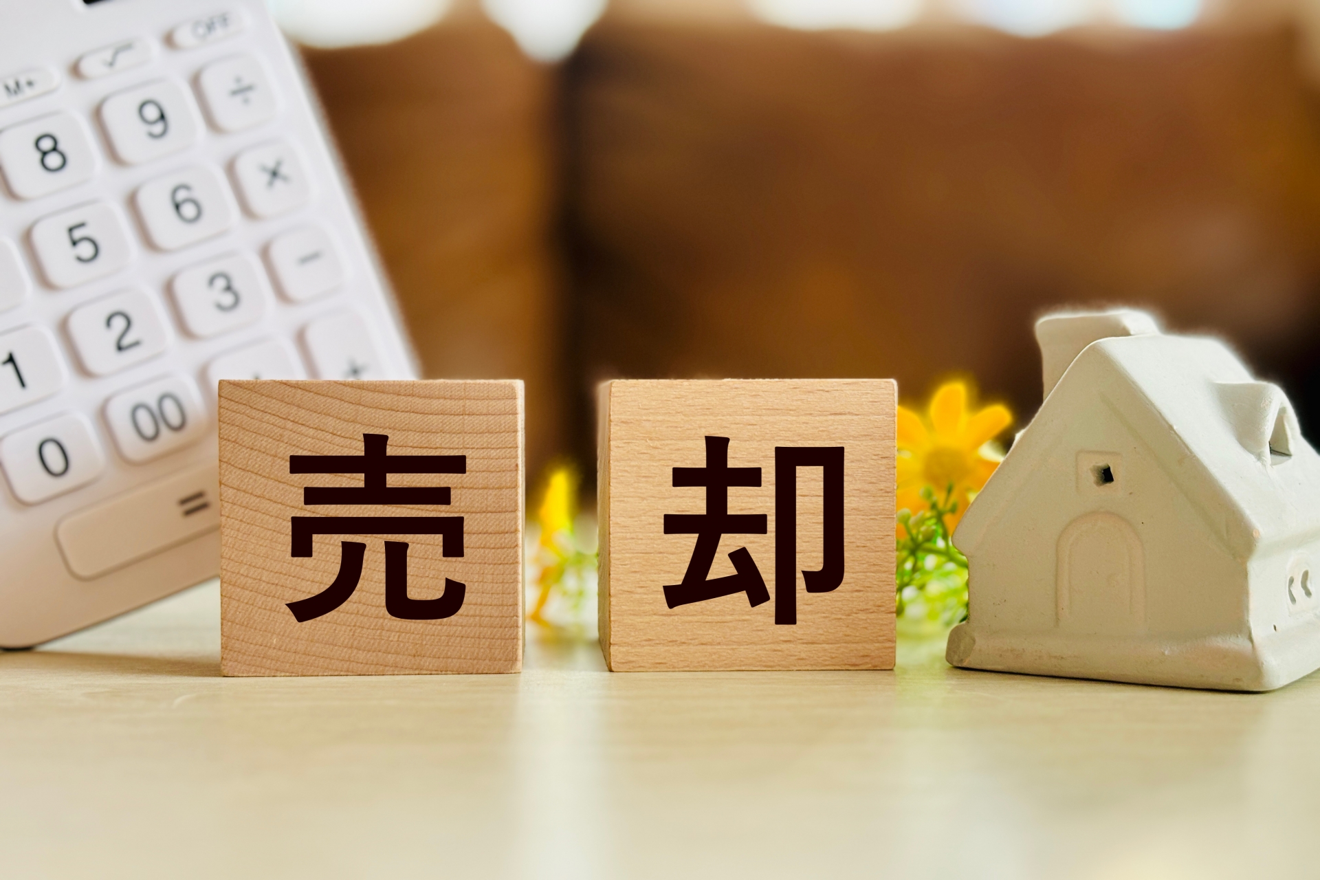 古い家を売却する際の計算をイメージした、電卓、木製ブロック、ミニチュアの家。