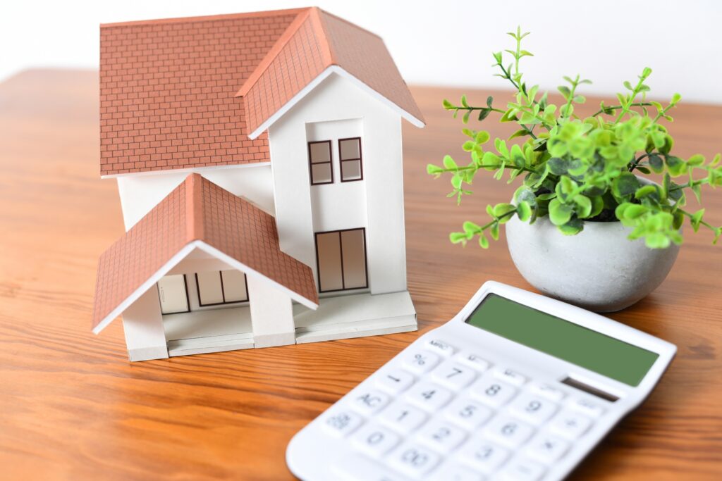 茶色の屋根の家の模型と電卓。離婚時の住宅ローン残債や財産分与を計算し、売却を検討する。