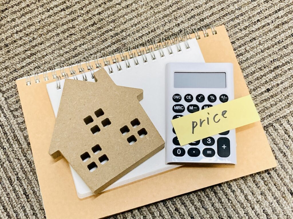 虫眼鏡と電卓で注文住宅の売却価格を査定し、市場情報をもとに適正な価格帯を把握する様子