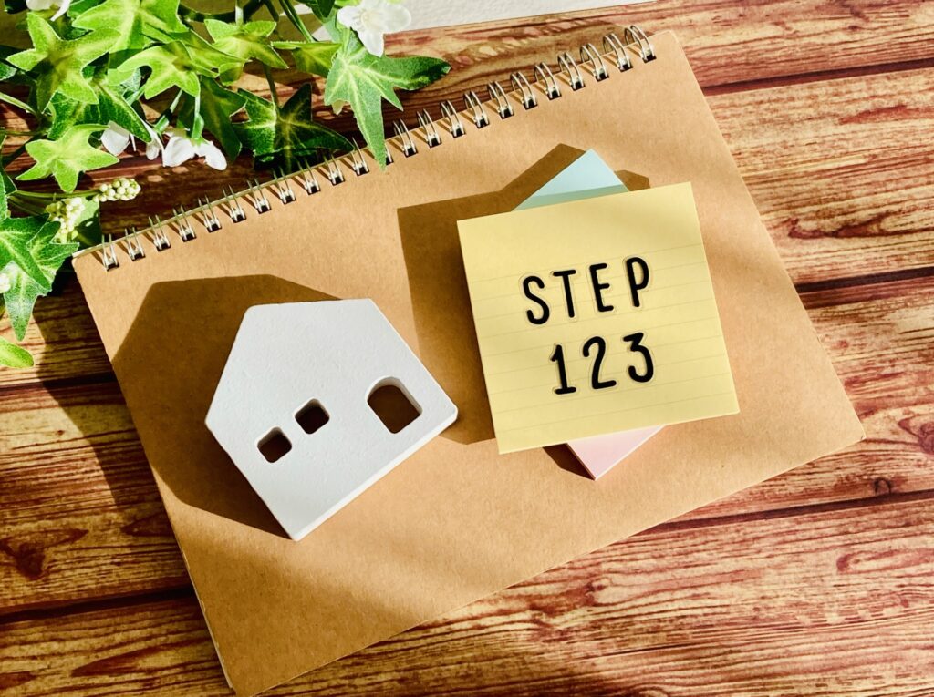 リングノートの上に置かれた白い家の形をした模型と、STEP123と書かれた黄色い付箋メモ。