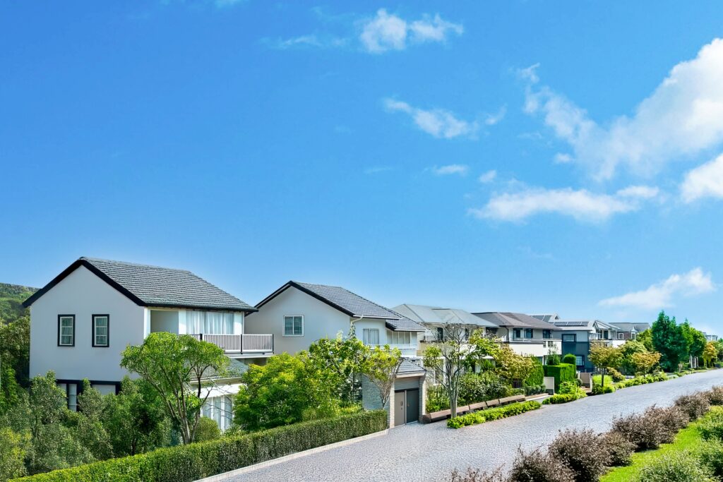 広々とした青空の下、整備された道路に沿って建つ、外観が統一されたモダンな一戸建ての住宅街。