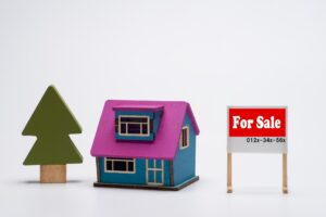 カラフルな注文住宅の模型とFor Sale（売却中）の看板。売却しにくい理由を暗示