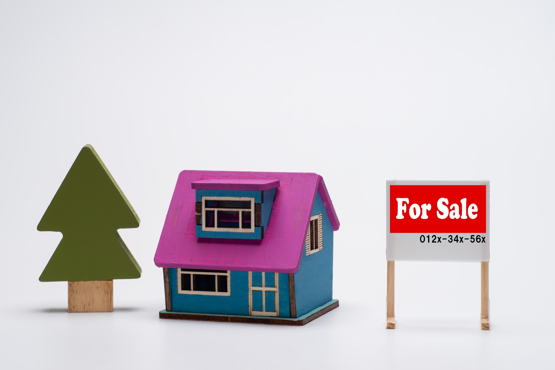 カラフルな注文住宅の模型とFor Sale（売却中）の看板。売却しにくい理由を暗示