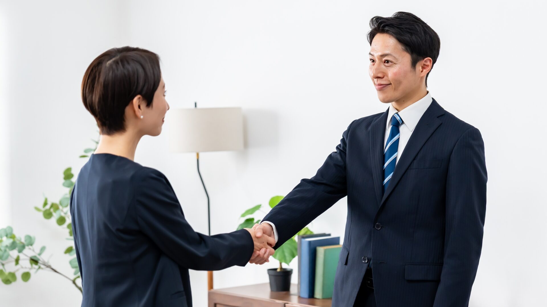 不動産売却の会社選びまたは契約時。スーツ姿の男女が営業担当者と売主として握手している