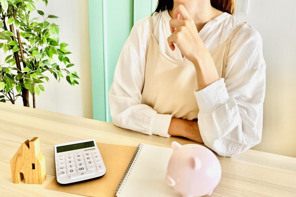 女性が電卓と家の模型を見ながら、離婚後の住宅ローンや残債、財産分与について思案する。