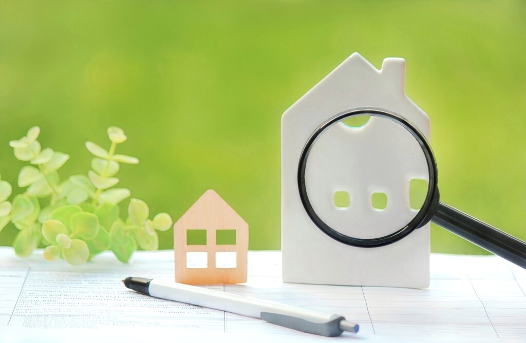 白い家の模型と小さな木の家の模型、そして家の窓部分を拡大する虫眼鏡