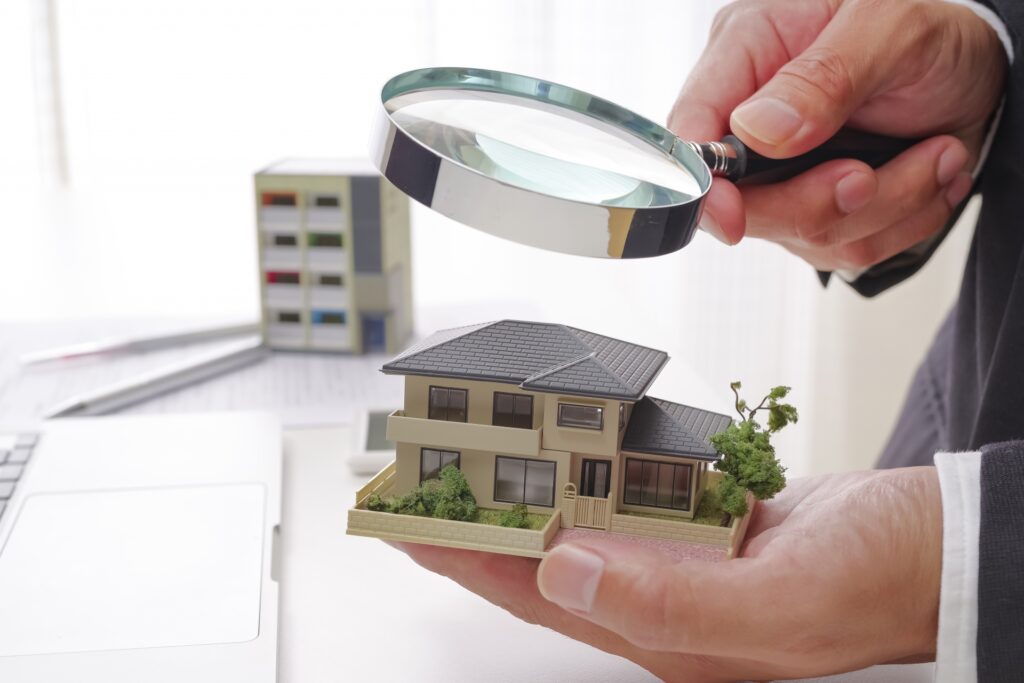 不動産の専門家が虫眼鏡を使い、家の模型を厳密に査定する様子。離婚時の売却額算定。