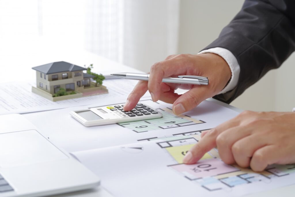 実家の売却費用や相場を計算する電卓と間取り図面および住宅模型