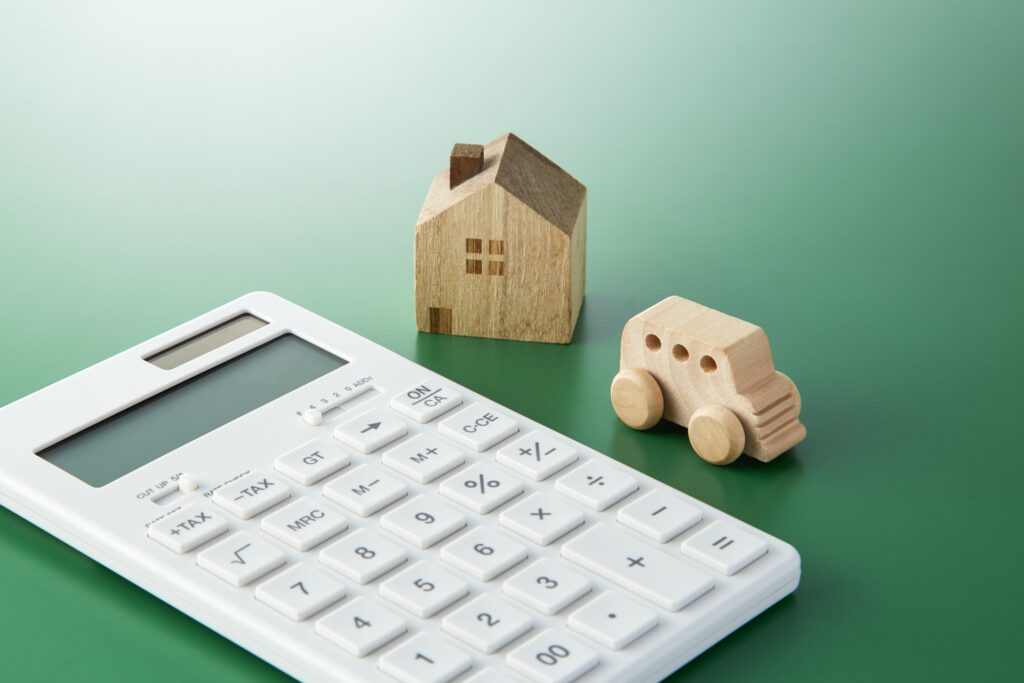 実家の売却益で住み替えや車の購入を検討する際の計算用電卓と木製の家・車のオブジェ