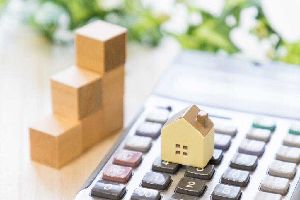 電卓のキーの上に小さな家の模型があり、奥には三段の階段状の積み木