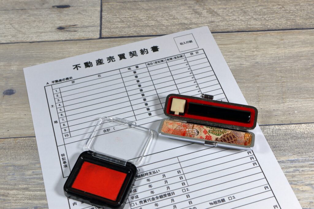 「不動産売買契約書」の書類の上に、朱肉と印鑑ケース。空き家の売却処分手続き