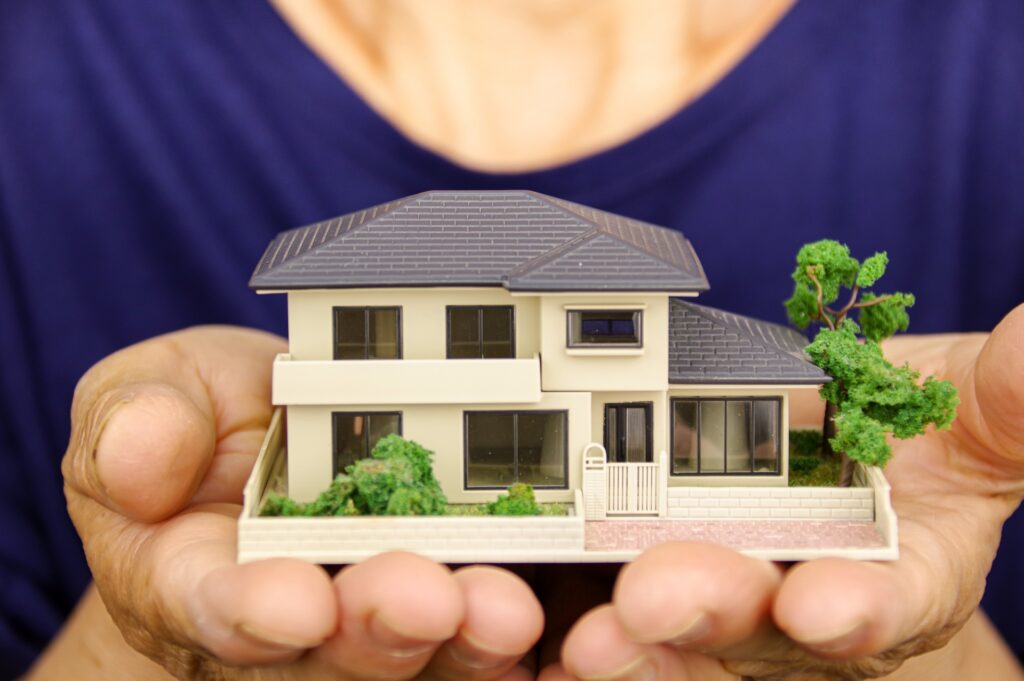 大切な実家の売却を慎重に検討するため、両手で包み込むように持つ一戸建ての模型