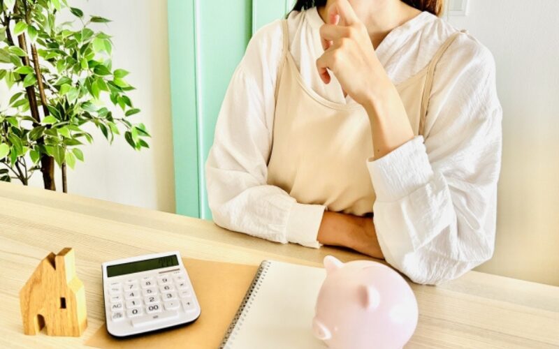 家を高く売る最適なタイミングや資金計画について、腕を組んで思案している様子の女性と電卓