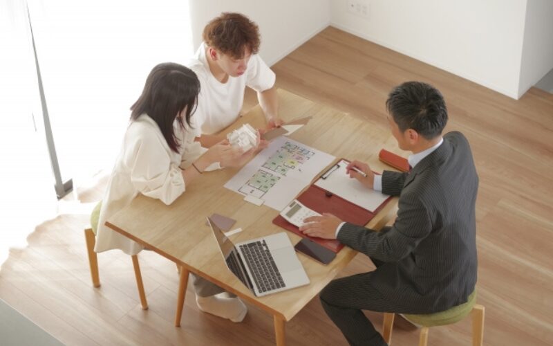 家を売るタイミングをプロに相談。不動産会社の担当者と間取り図を見ながら話し合う若い夫婦
