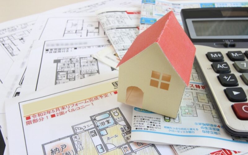 住み替えで家が売れない時に売却の対処法を考える、赤い家の模型と宣伝チラシ