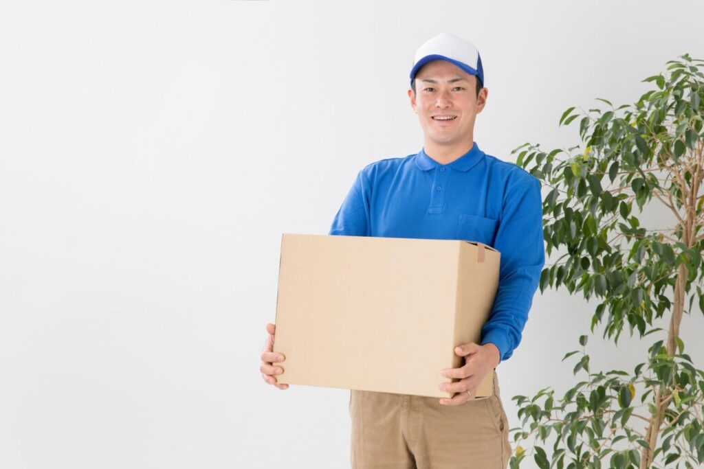 不動産売却後の引っ越し費用を連想させる、段ボール箱を持つ運送会社の配達員。
