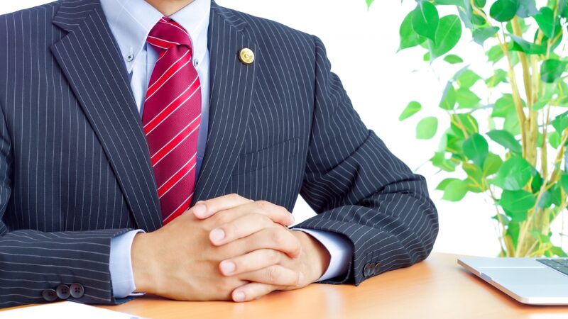不動産売却の悩みを法律や専門的な視点で解決する専門家。スーツ姿でデスクに座り相談に乗る弁護士のイメージ。
