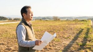 初めての土地売却で失敗しないために、売却予定の更地へ足を運び、手元の書類を見ながら注意点を確認するオーナー。