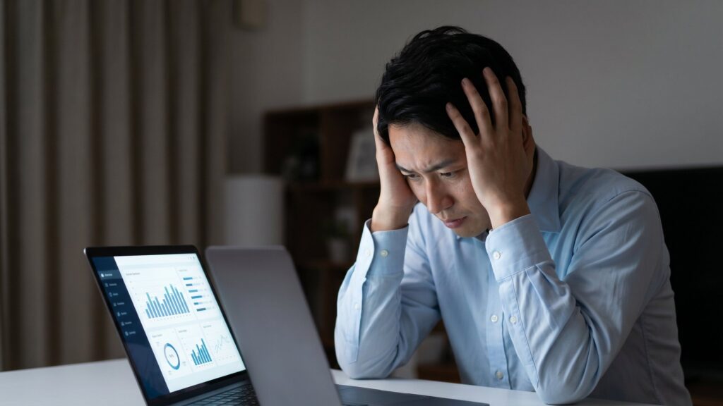不動産売却で家が売れないストレスを解消するため、パソコンでデータ分析を行うものの、具体的な原因や対策が見つからず悩む男性。
