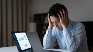不動産売却で家が売れないストレスを解消するため、パソコンでデータ分析を行うものの、具体的な原因や対策が見つからず悩む男性。